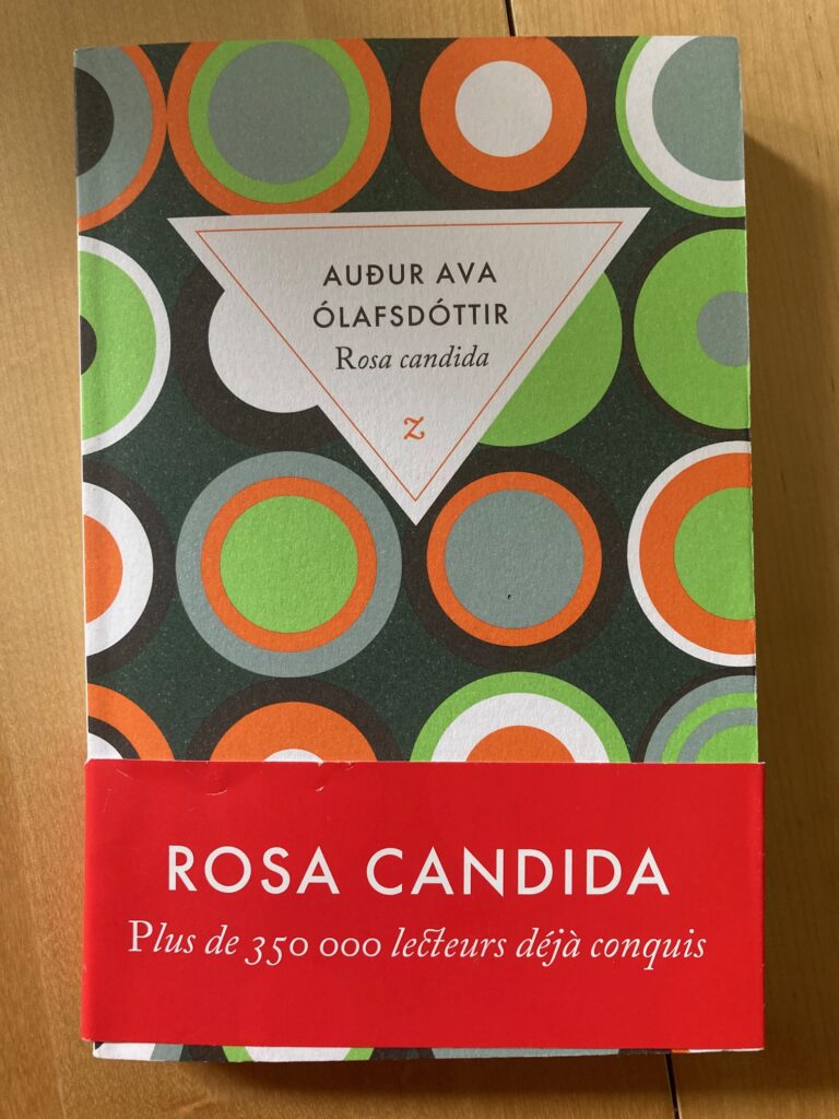 Photo du livre Rosa Candida de Auður Ava Ólafsdóttir. La couverture est vert foncé avec des cercles de couleur orange, vert pomme, gris clair et gris foncé. Il y a un bandeau rouge qui dit "Rosa Candida plus de 350 000 lecteurs déjà conquis".